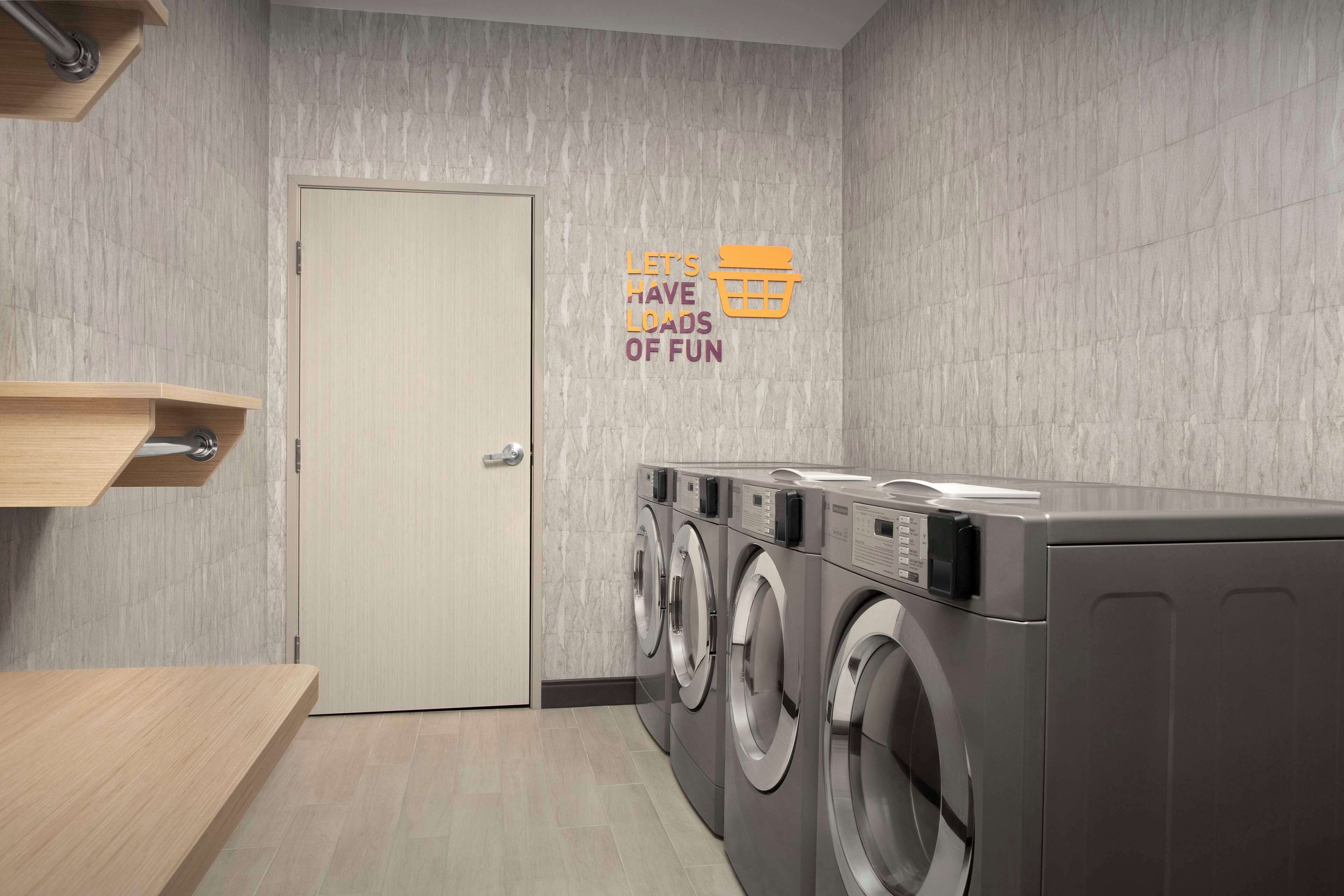 A laundry room with three front-loading washing machines, a wooden bench, and a door.