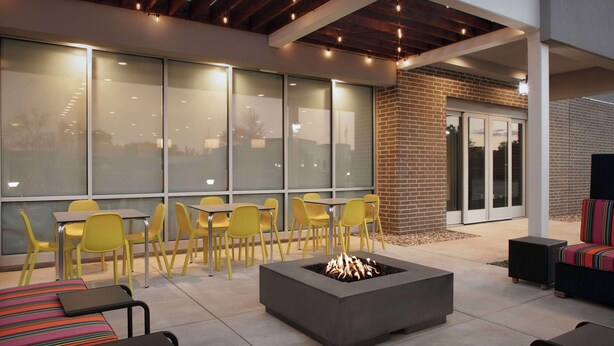 An outdoor seating area with yellow chairs, a fire pit, and a covered patio. - Home2 Suites By Hilton Georgetown Austin North (Georgetown)