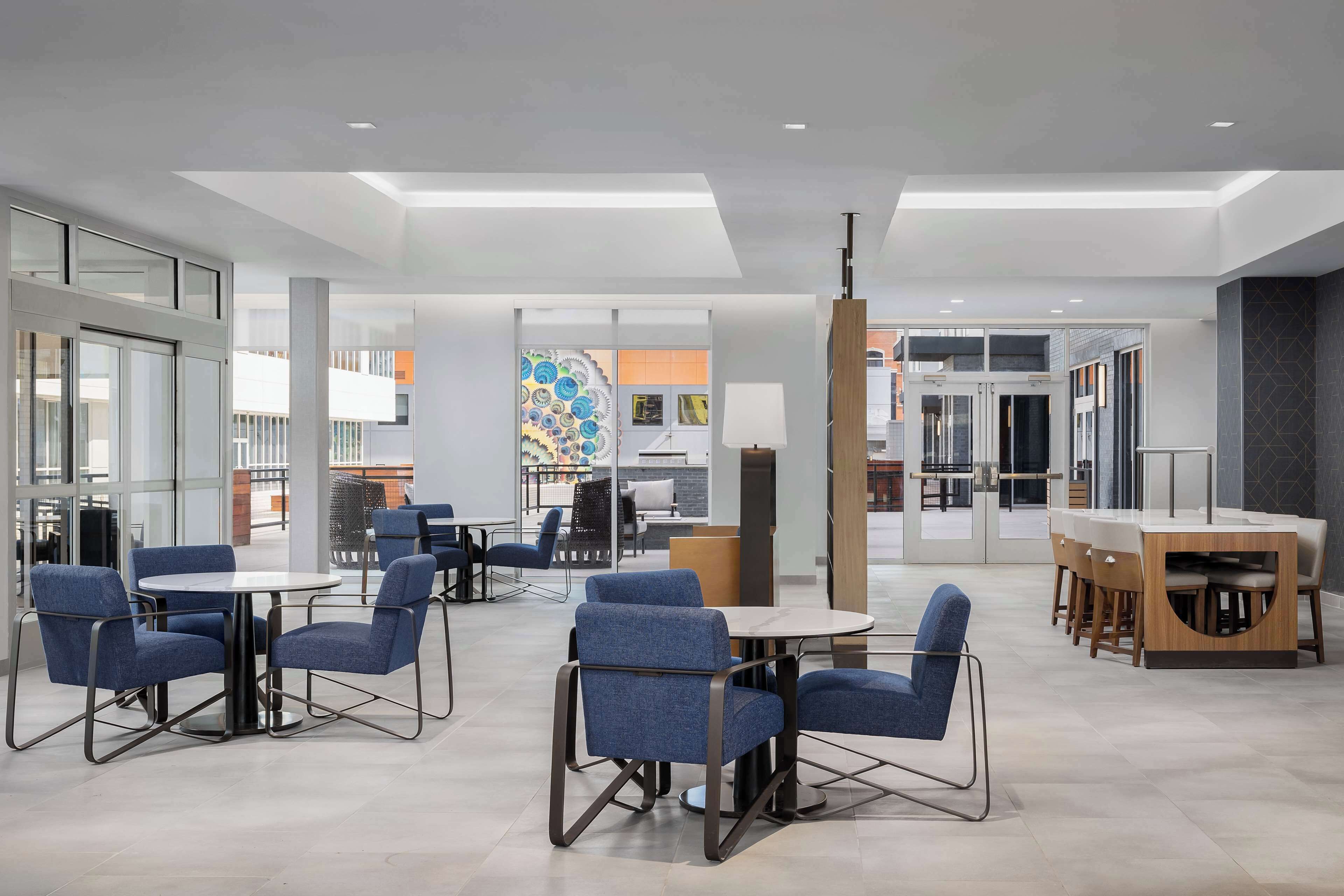 A modern indoor space with round tables and blue chairs, featuring glass partitions and a central decorative element.