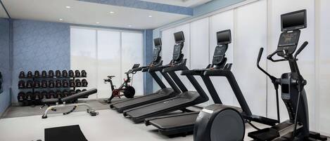 Une salle de sport équipée de tapis de course, d’un vélo d’appartement, d’haltères et d’un tapis de sol.