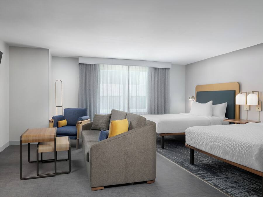 Een hotelkamer met een bank, fauteuil en een bed. Er is een televisie aan de muur bevestigd en een raam met gordijnen.