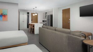 A modern hotel room with a sofa, two single beds, a dining area, a kitchen, and a TV. - Homewood Suites By Hilton Newport Cincinnati (Newport)