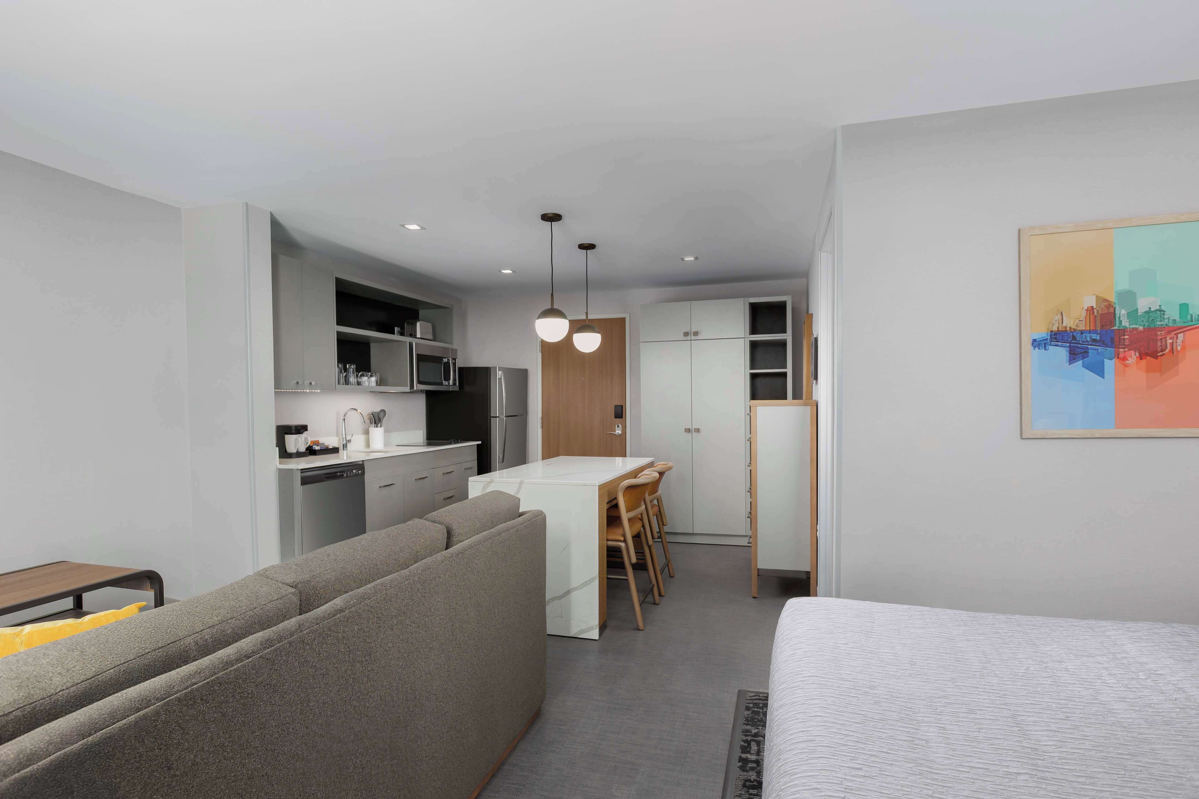 A compact hotel room with a kitchenette, a sofa, a bed, and a dining area.