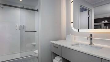 Une salle de bain moderne avec une douche à parois de verre, un lavabo blanc avec un miroir et des serviettes soigneusement pliées.