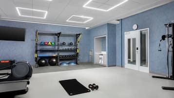 A gym with exercise equipment, a black mat, and a wall-mounted rack with dumbbells.