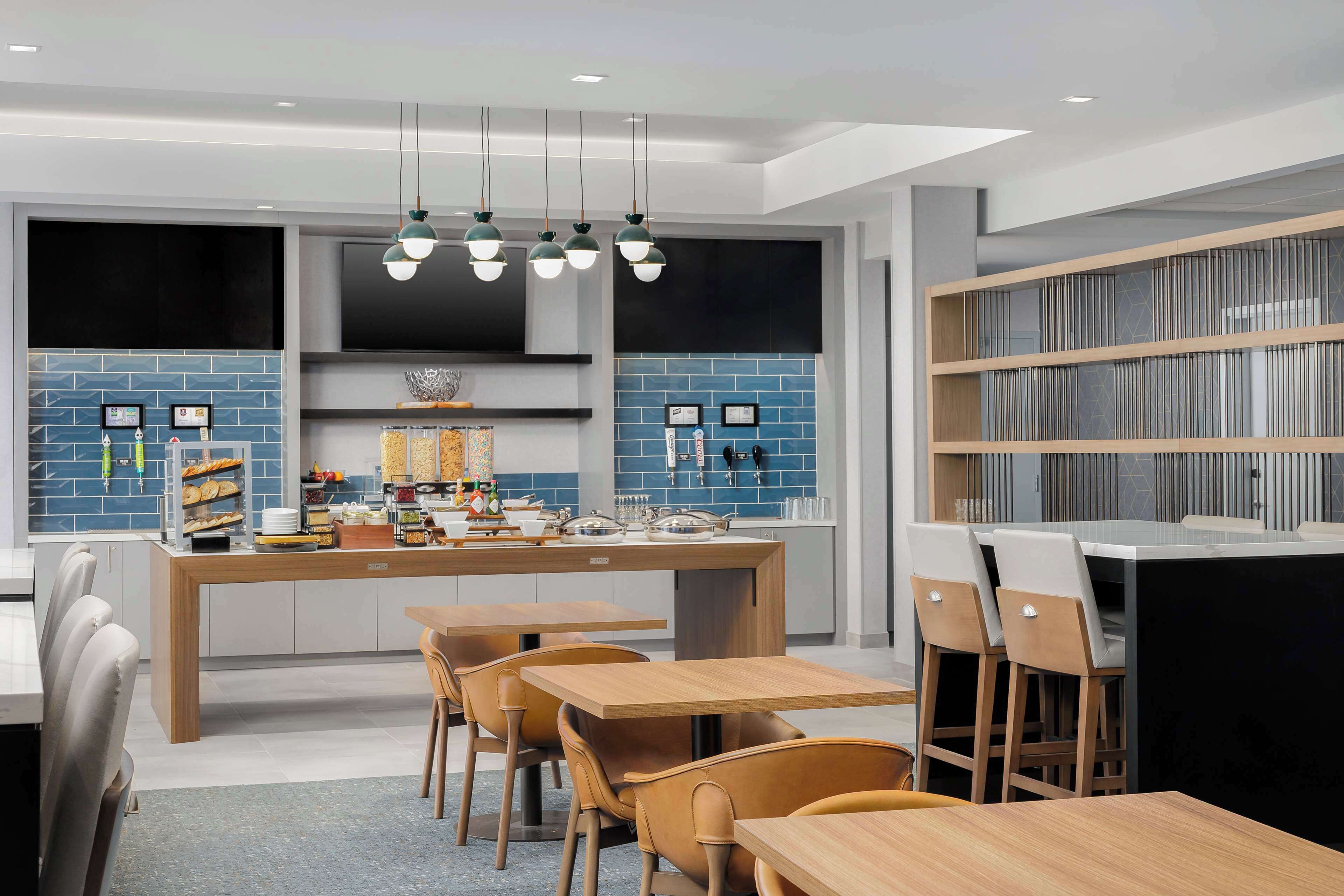Una cocina moderna con una isla central, electrodomésticos integrados y una zona de estar con mesas y sillas de madera.