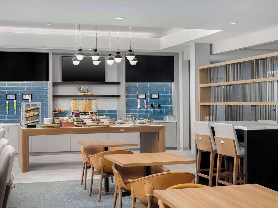 Una cocina moderna con una isla central, electrodomésticos integrados y una zona de estar con mesas y sillas de madera.