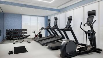 Een sportschool met loopbanden, gewichten en een hometrainer.