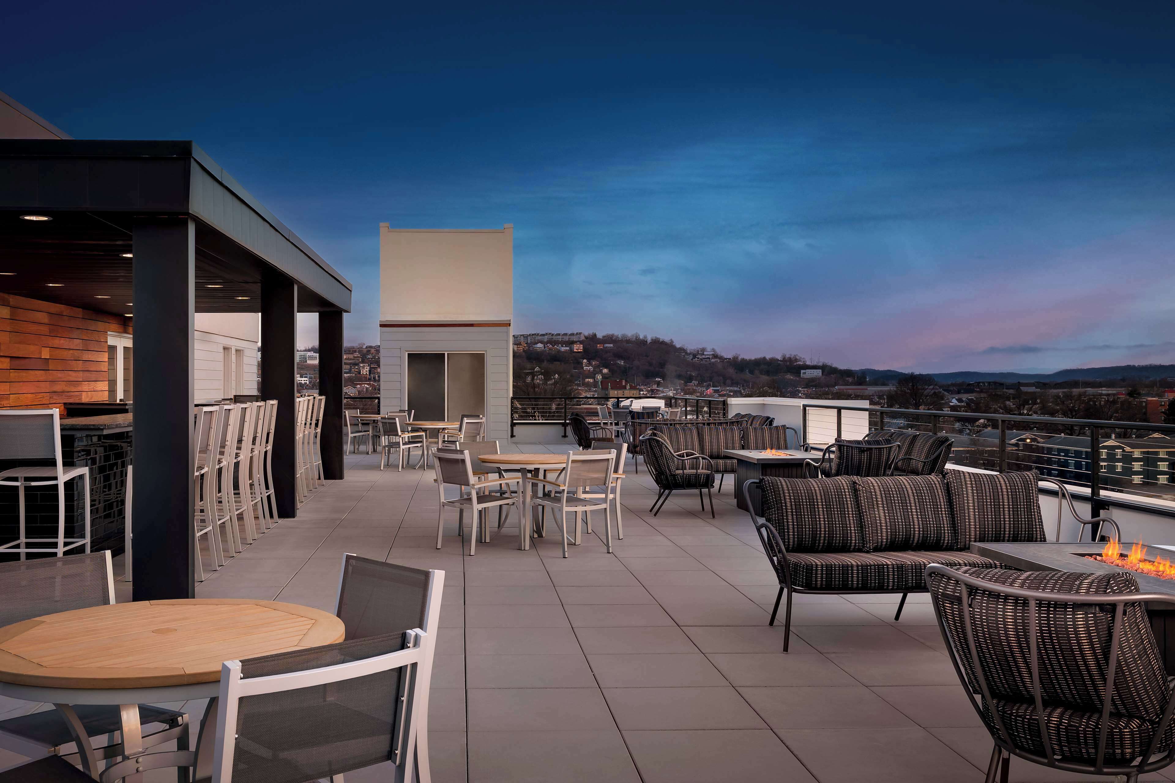 A rooftop terrace with outdoor seating, a fire pit, and a view of the cityscape.