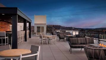 A rooftop terrace with outdoor seating, a fire pit, and a view of the cityscape.