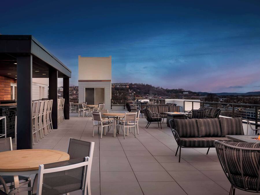 A rooftop terrace with outdoor seating, a fire pit, and a view of the cityscape.