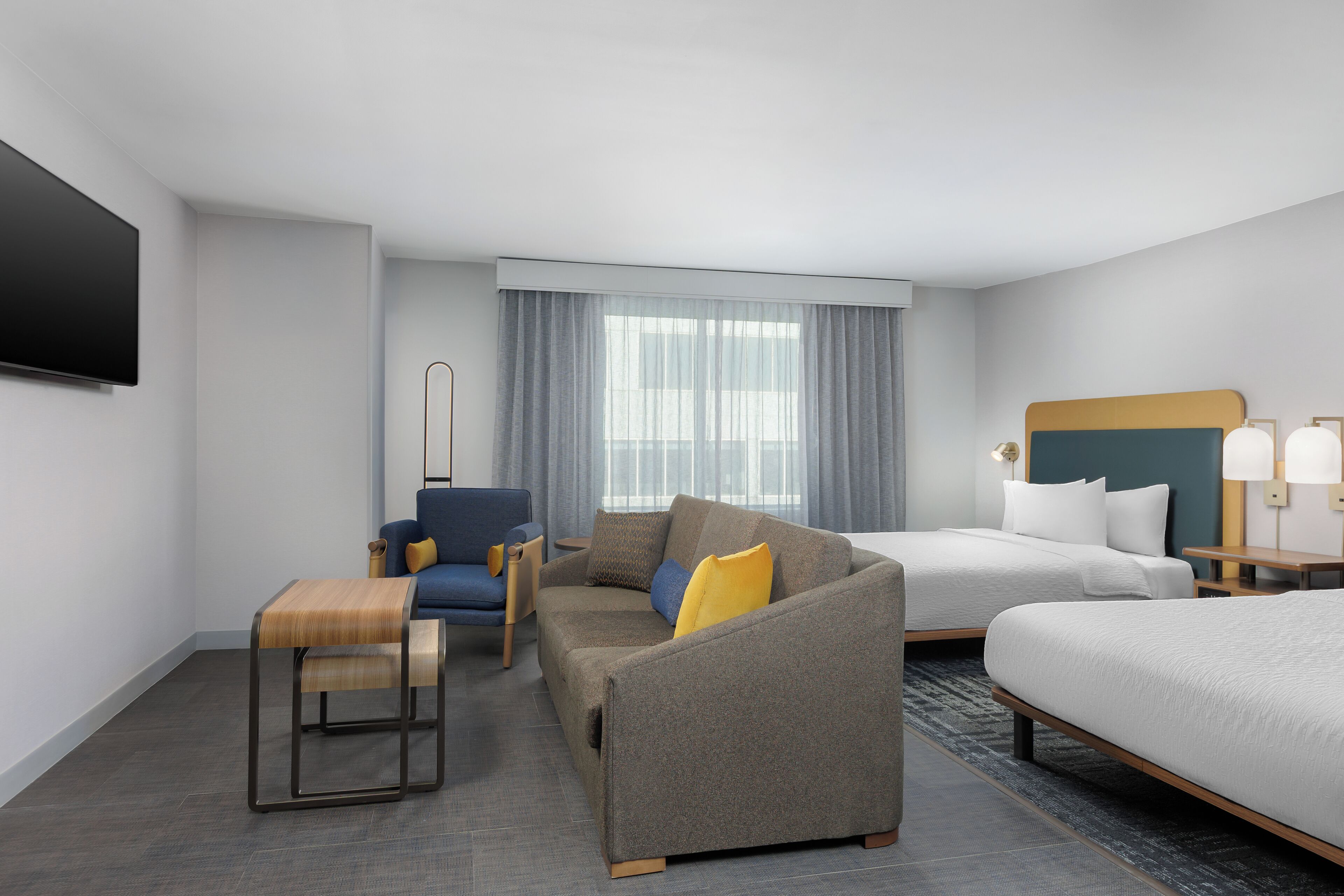 Una habitación de hotel moderna con sofá, sillón, cama y televisión de pantalla plana.