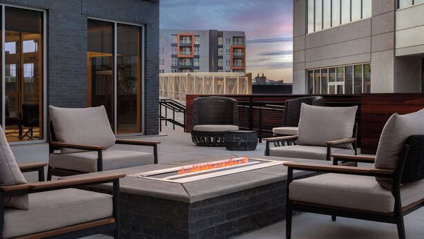 A rooftop patio with outdoor seating, a fire feature, and a view of a modern building. - Homewood Suites By Hilton Newport Cincinnati (Newport)
