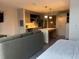 Una habitación de hotel moderna con sofá, cama, kitchenette y un área de comedor separada.