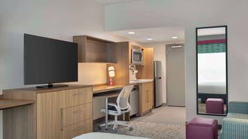 A modern hotel room with a bed, a desk with a computer, a television, a microwave, and a small seating area.