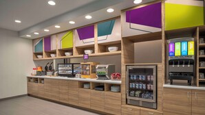 Un espace moderne en libre-service où l’on peut prendre son petit-déjeuner, avec un choix varié d’aliments, un distributeur de boissons et un espace réfrigéré.