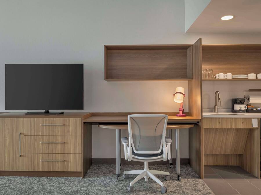 A modern office space with a desk, chair, television, and built-in shelving.