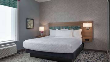 A hotel room with a large bed, two bedside lamps, a wall-mounted heater, and a window with blinds.