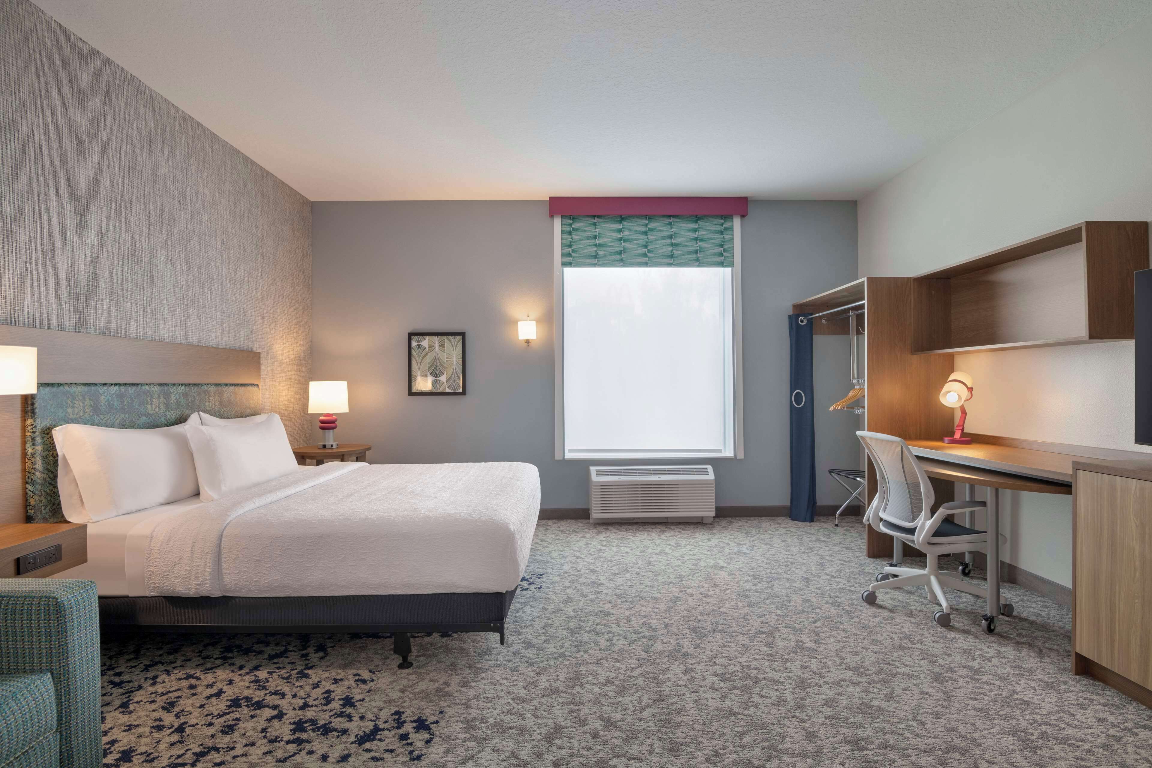 Habitación de hotel con cama, escritorio, silla y un ventanal con vistas.