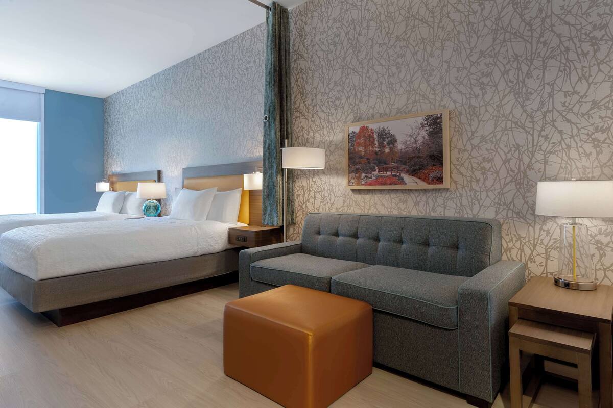 Ein Hotelzimmer mit Bett, einer Couch, einem Hocker, einem Nachttisch und einer Lampe.