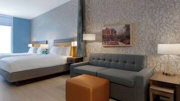 A hotel room with a bed, a sofa, an ottoman, a nightstand, and a lamp.