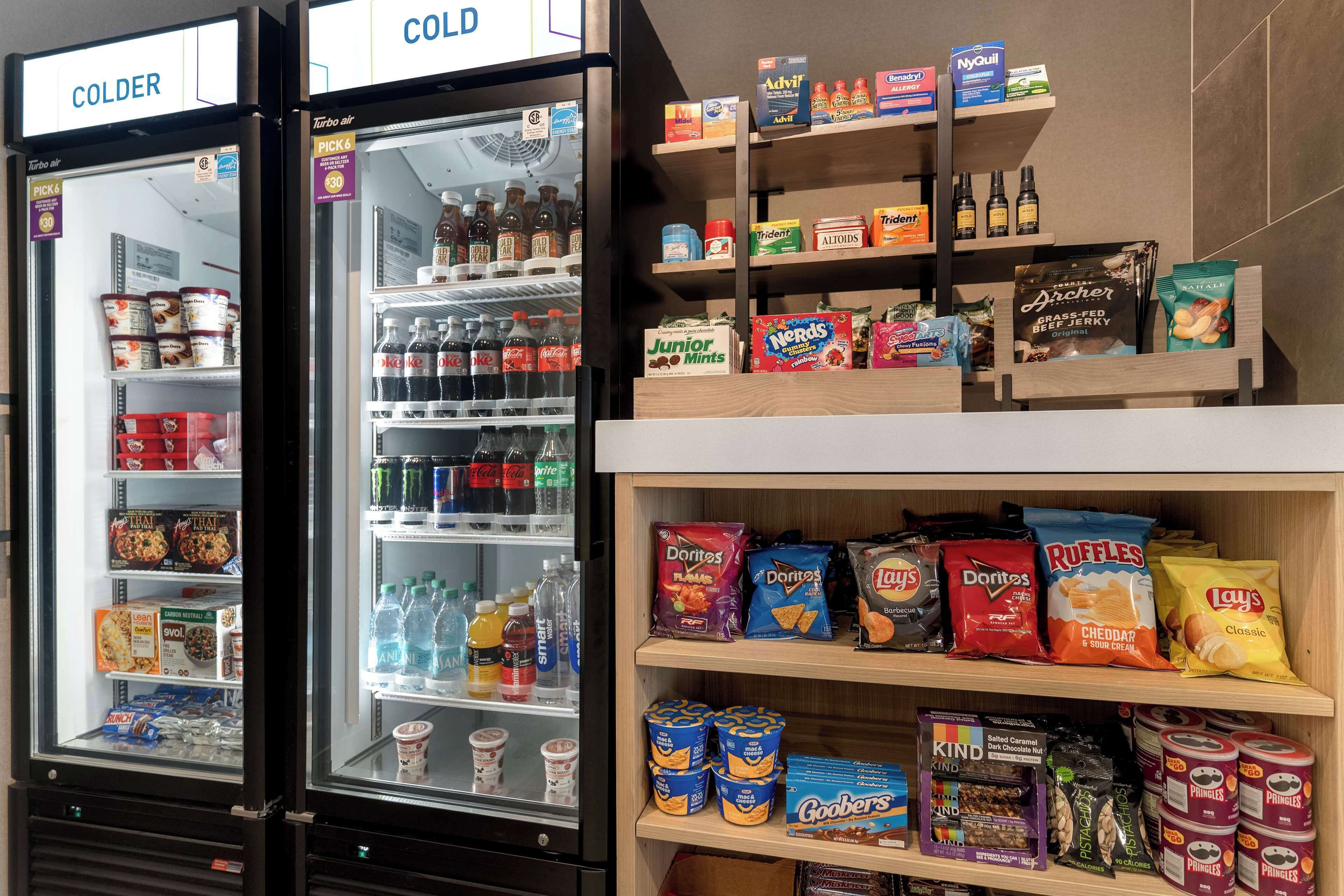 Een gekoelde vitrine met diverse drankjes en snacks, waaronder Coca-Cola, energydranken en Doritos.