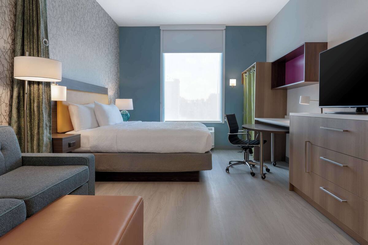 Ein modernes Hotelzimmer mit Bett, Schreibtisch, Fernseher und Sitzgelegenheit.