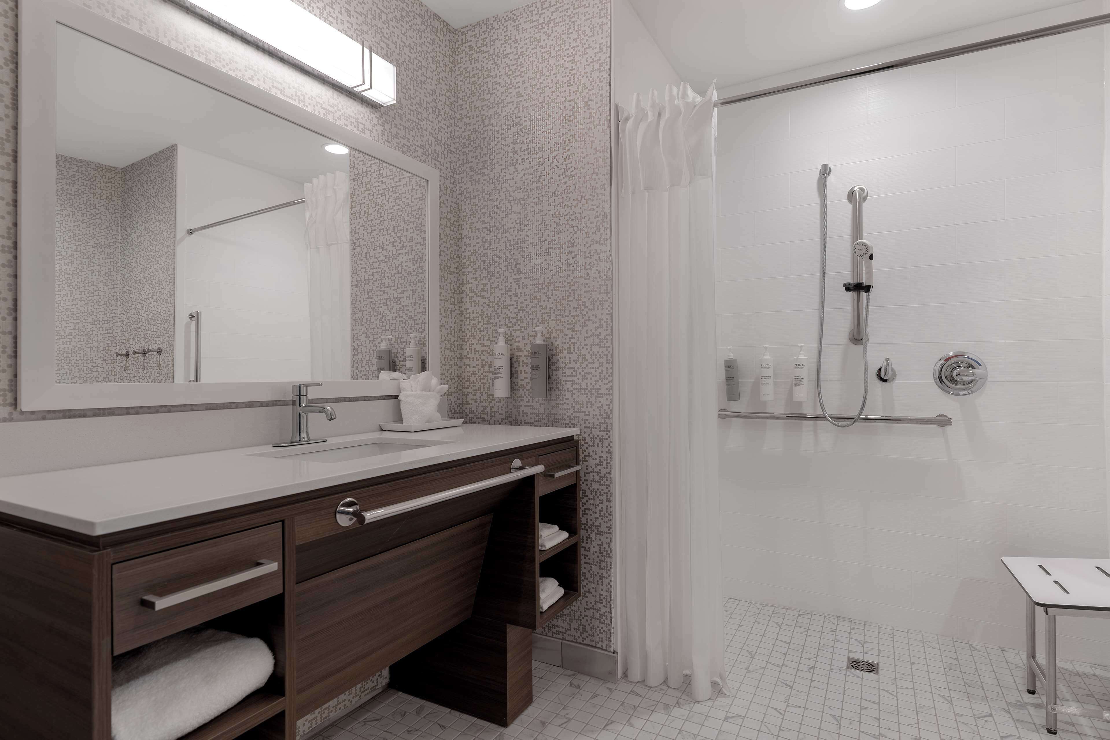 A modern bathroom with a large mirror, a shower with a glass door, and a vanity with a sink and storage drawers.