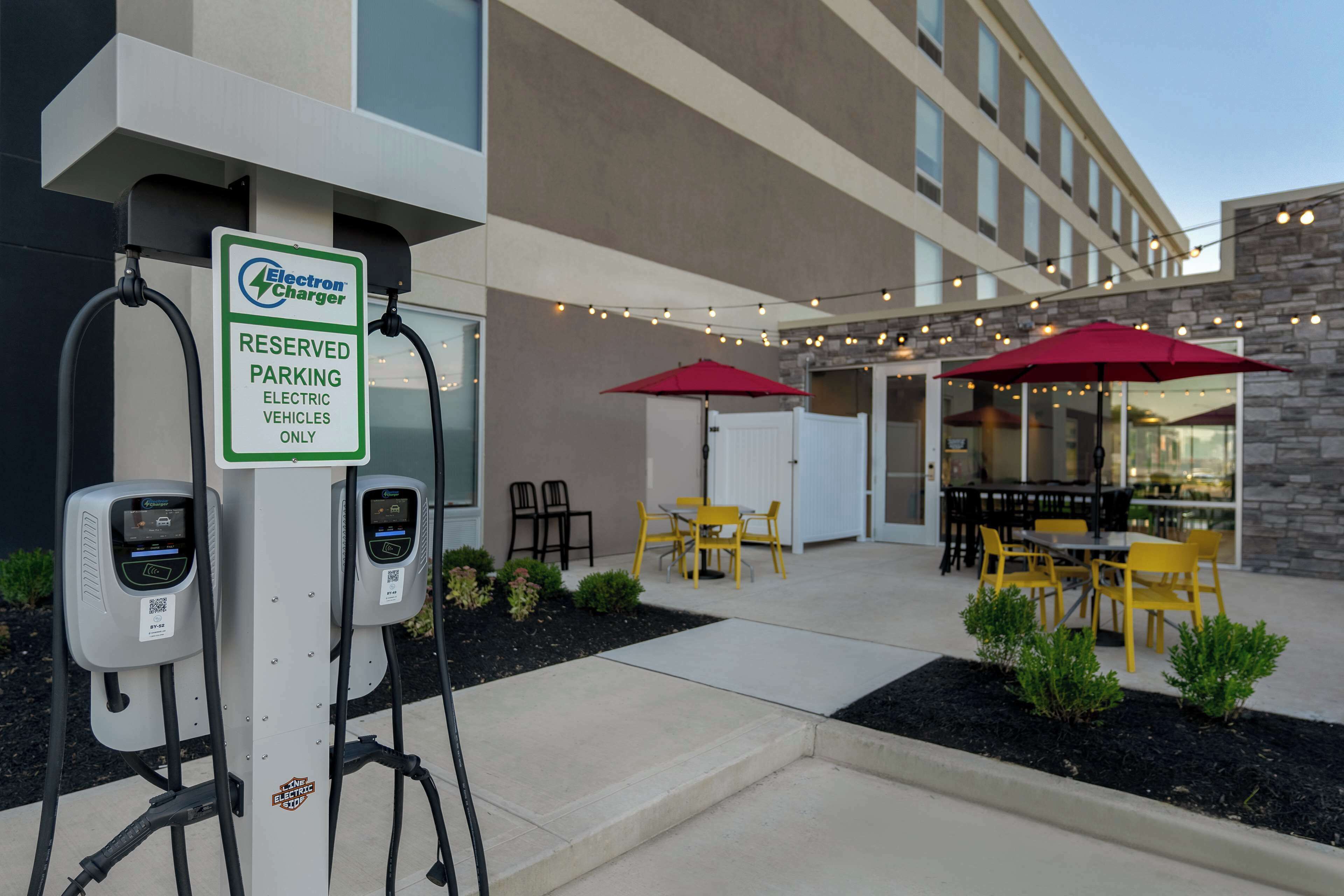 Un hotel con un patio al aire libre que cuenta con sillas amarillas, sombrillas rojas y una estación de carga para vehículos eléctricos.