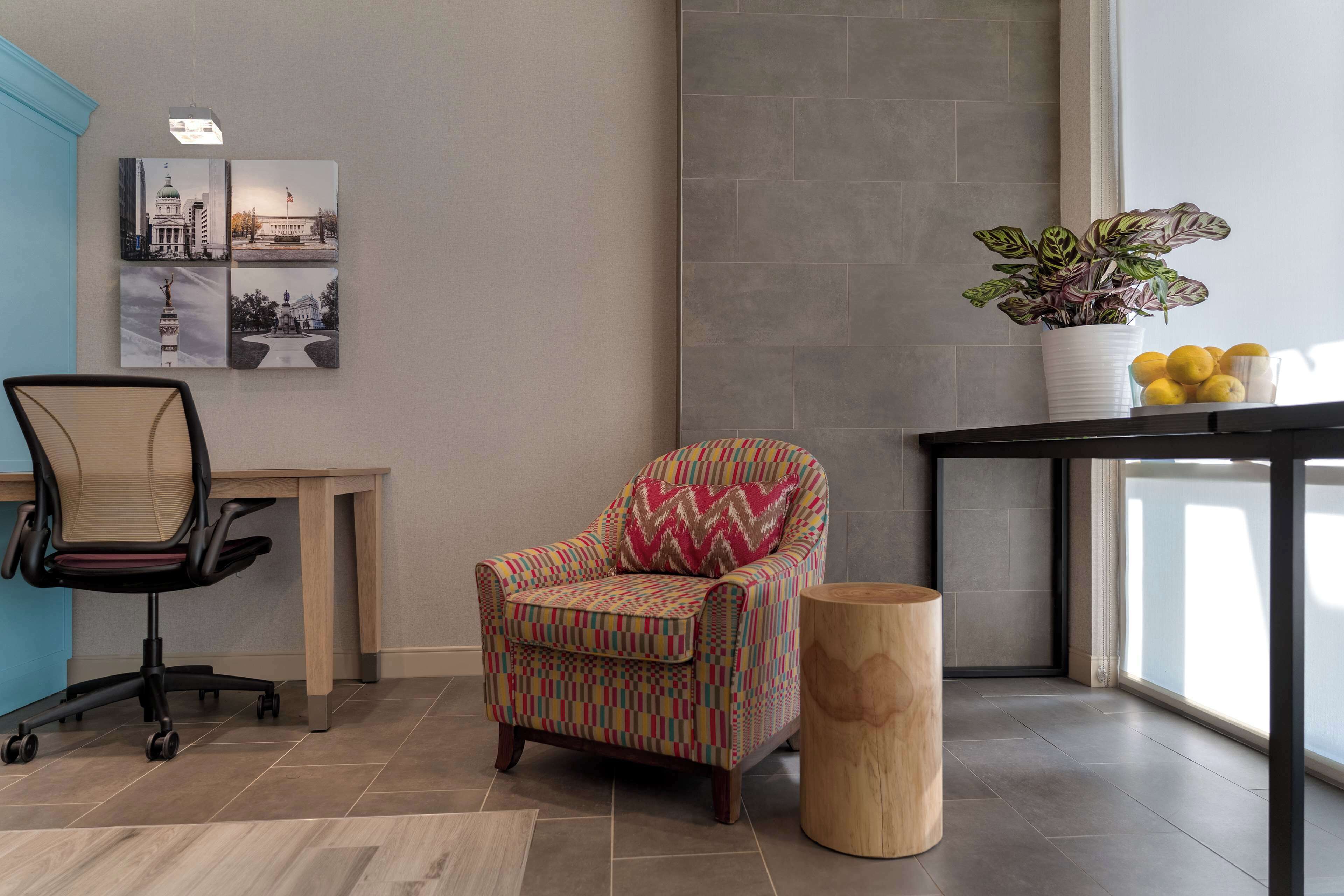 A modern office space with a colorful armchair, a wooden side table with a plant, and a desk with a chair.