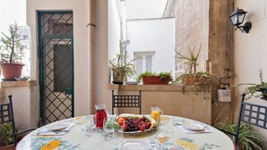 A round table with a floral tablecloth, set with plates, cutlery, and a fruit platter.