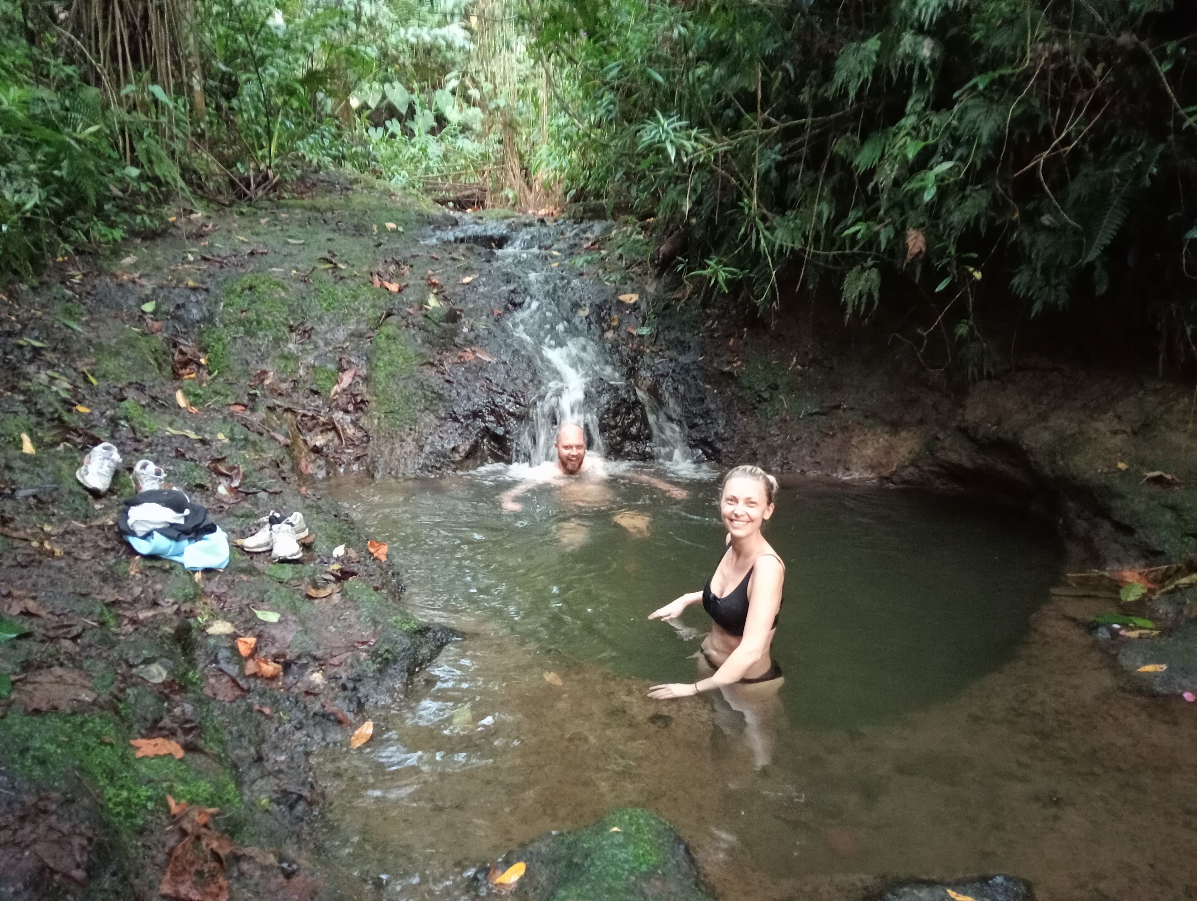 Eine natürliche Umgebung mit einem kleinen Wasserfall und einer Person, die im Wasser sitzt.