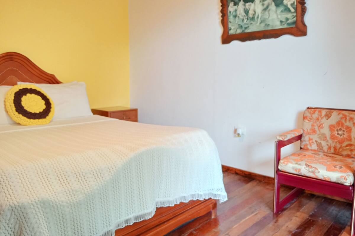 Une chambre à coucher avec un lit, une table de chevet, une chaise et un tableau accroché au mur.