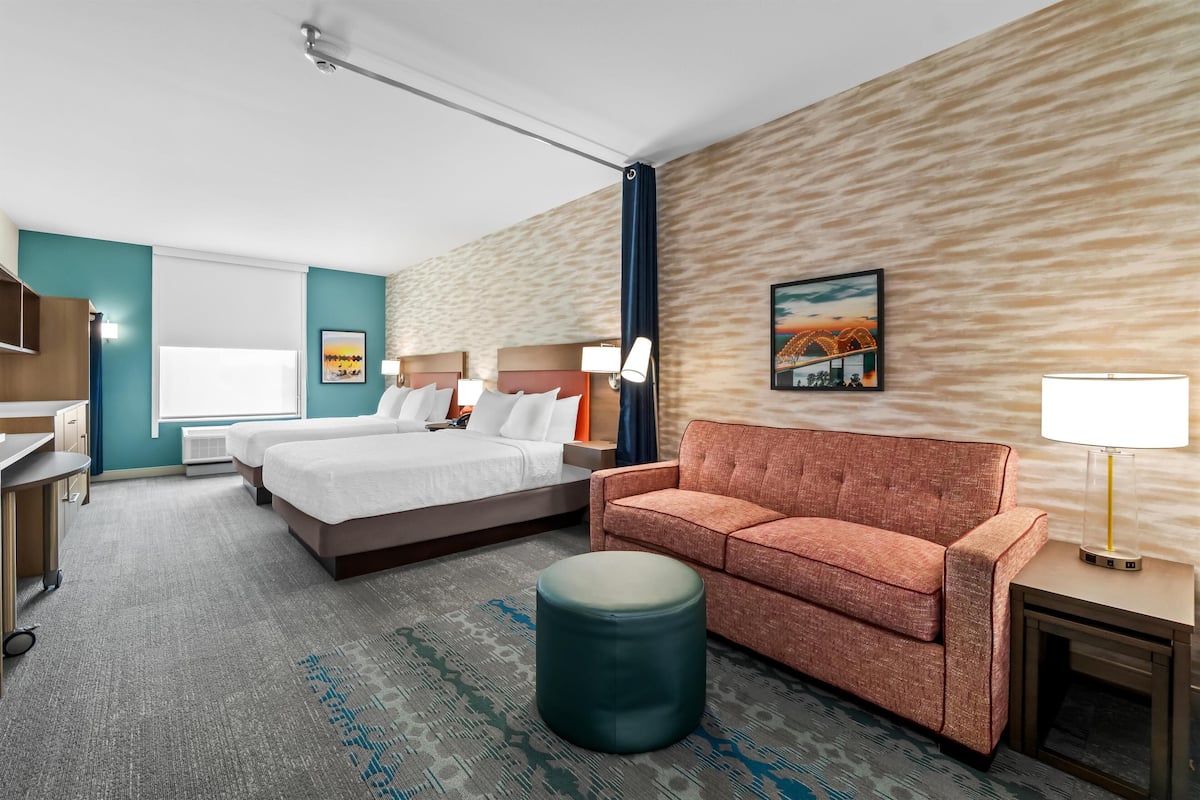 A hotel room with a bed, a sofa, a desk, and a lamp.