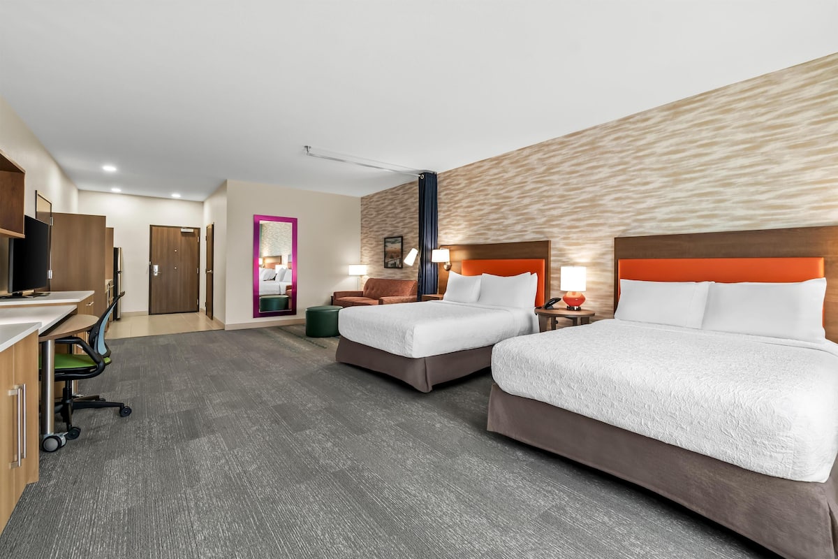A hotel room with two beds, a desk, a chair, and a TV.