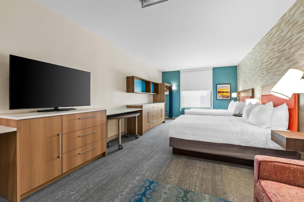 A hotel room with a bed, a desk with a flat-screen TV, a wardrobe, and a bathroom with a shower.