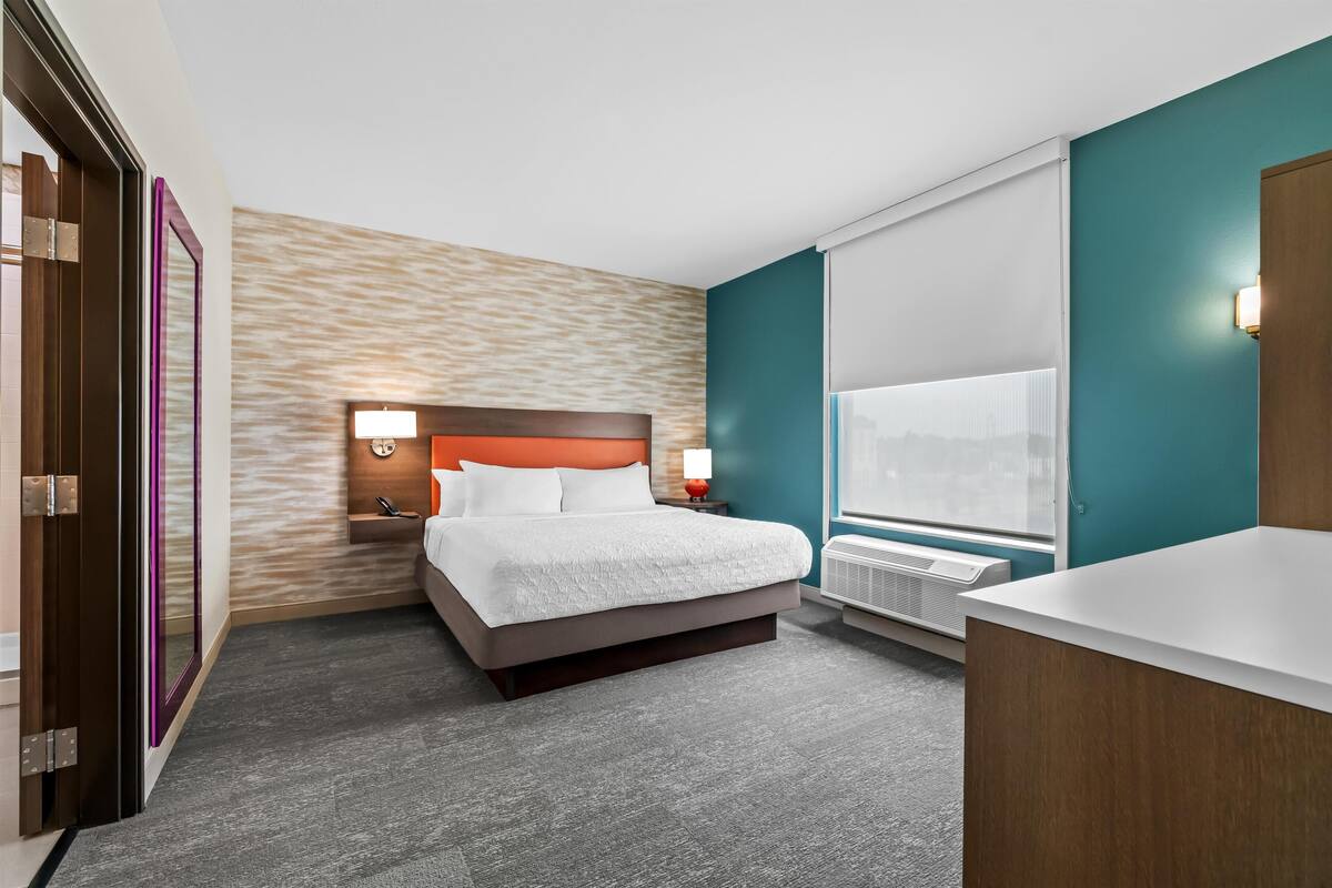A hotel room with a bed, bedside table, lamp, and window.