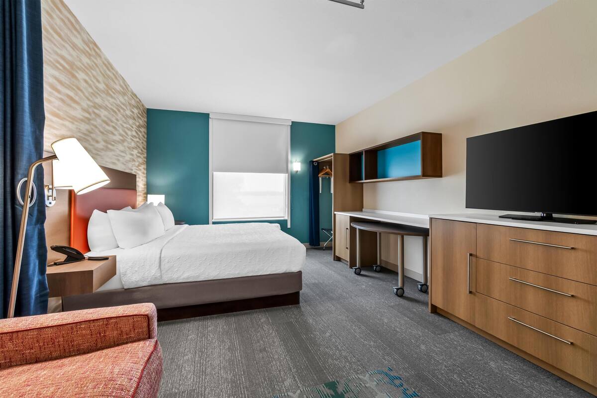 A hotel room with a bed, desk, TV, and a wardrobe.