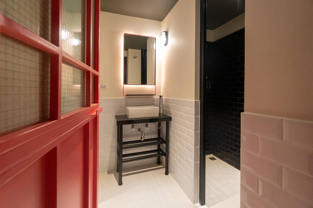 Un baño con un lavabo blanco, un espejo y una ventana con marco rojo.