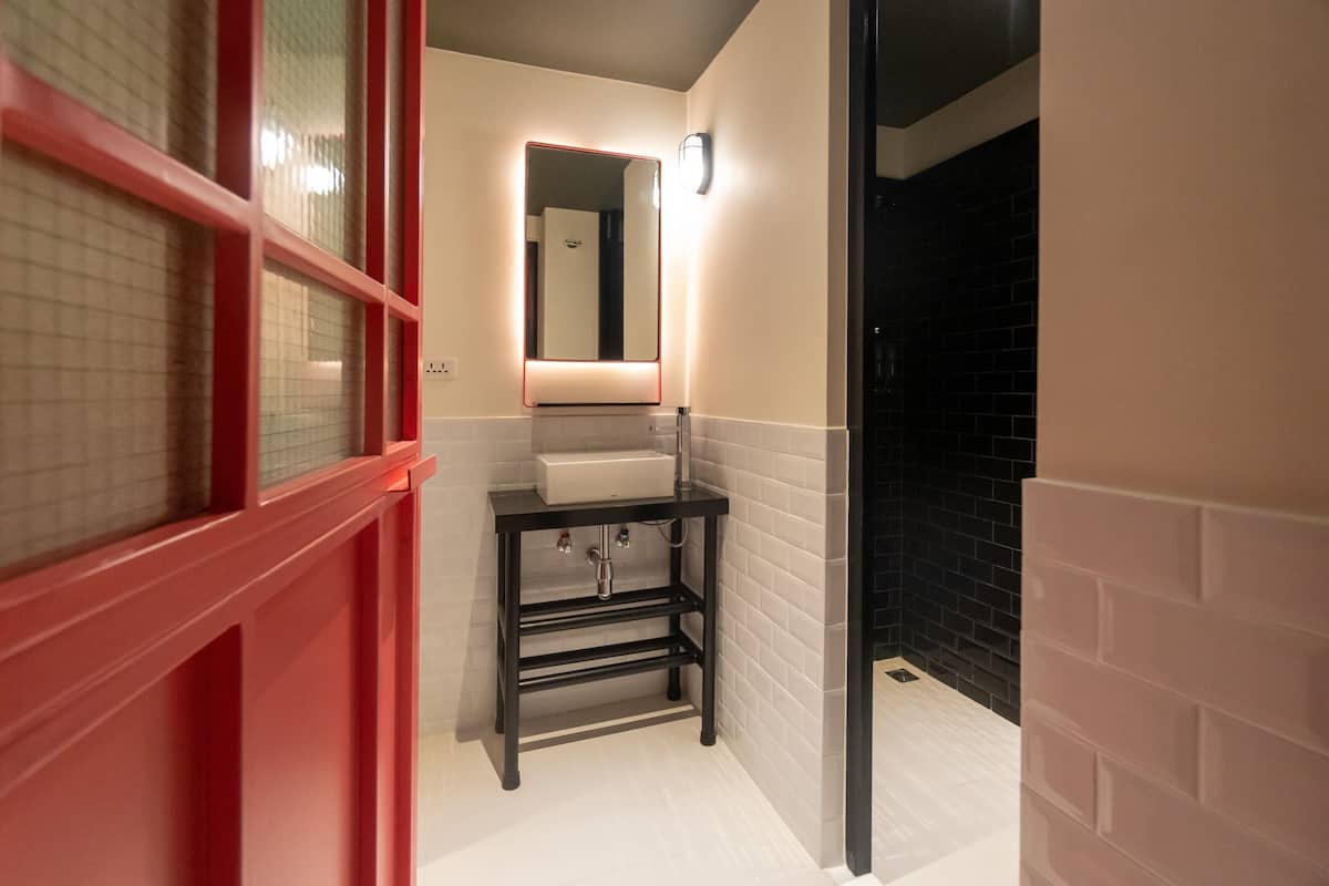 A bathroom with a white sink, a mirror, and a red-framed window.