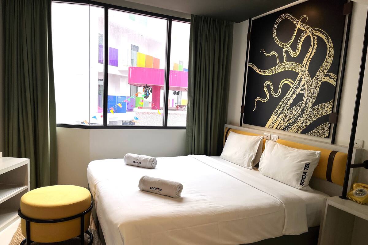 Una habitación de hotel con una cama, un ventanal con cortinas, un reposapiés amarillo y una pared con dise ño negro y dorado.