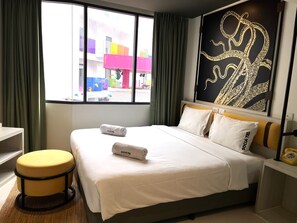 Una habitación de hotel con una cama, un ventanal con cortinas, un reposapiés amarillo y una pared con diseño negro y dorado.