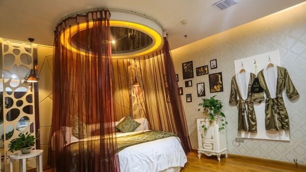 Ein Bett mit Himmelszelt, ein Nachttisch in Weiß, ein kleiner Blumentopf und eine Wand mit gerahmten Bildern.