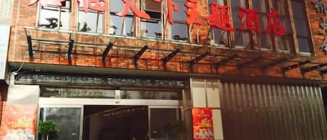 A building with a sign in a foreign script, a glass entrance, and a potted plant outside.