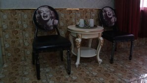 Ein Zimmer mit einem fußbodenartig befliessten Boden, zwei Stühle mit runden Rückenlehnen, einem kleinen runden Tischchen mit Tablett und einer Wand mit einer dekorativen Verkleidung.