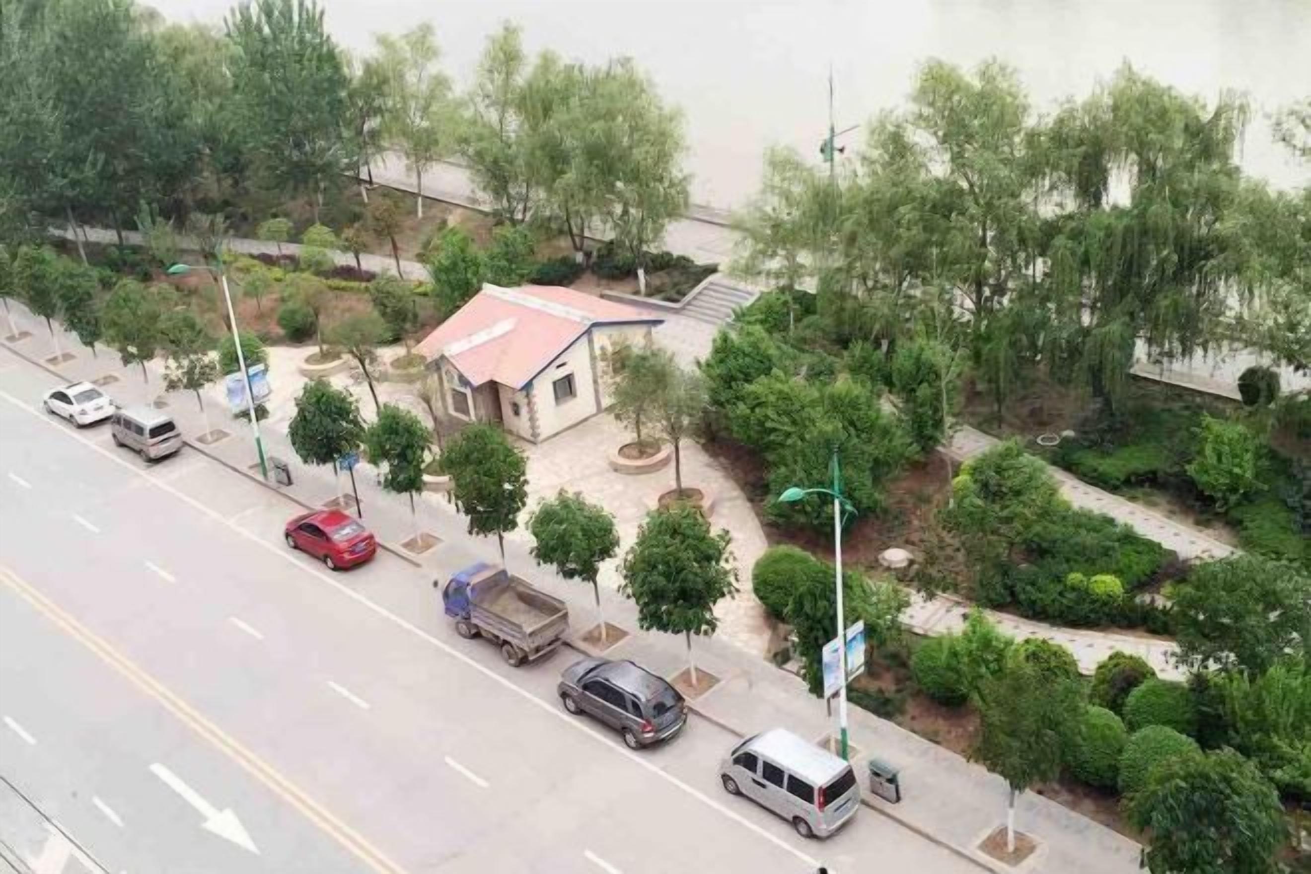 A road with parked cars and a building with a red roof.