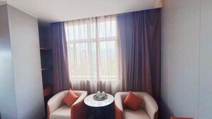 Ein Eckzimmer mit zwei Sofas, einem kleinen runden Tisch und einem großen Fenster mit Vorhängen.