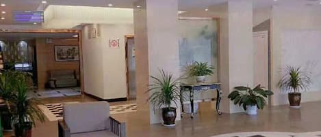 A hotel lobby with a checkered floor, seating area, and potted plants.