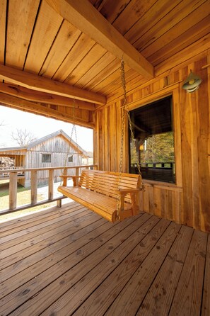 Une cabane en bois avec une véranda, une balançoire et une vue sur un autre bâtiment en bois situé à l’extérieur.