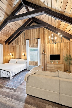 A cozy attic bedroom with a bed, a sofa, a TV, and a candelabra.